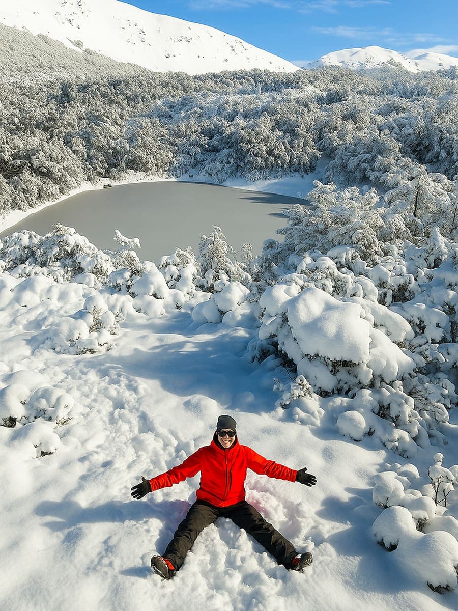 La laguna congelada del Refugio Neumeyer, con una persona de campera roja al borde y los arbustos cubiertos de nieve.