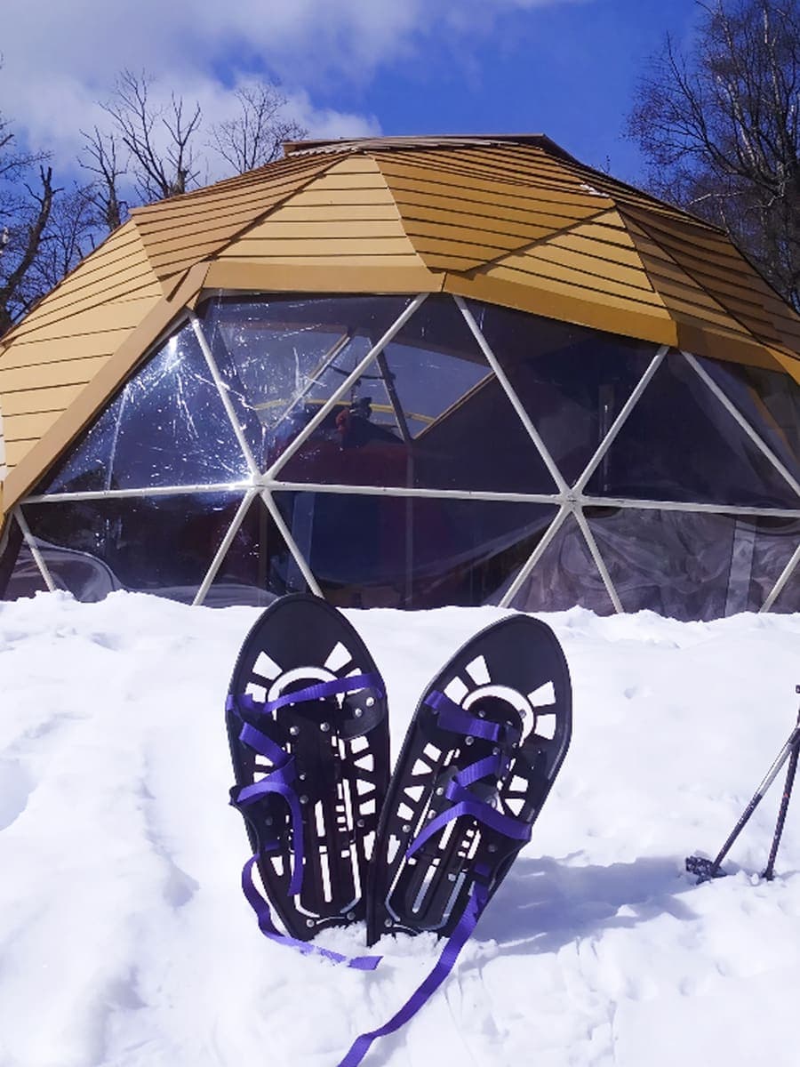 Un par de raquetas de nieve apoyadas en la nieve, con el domo del refugio detrás.